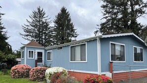 A single-story mobile home with a blue exterior and white trim. It features a front porch with a small staircase and a covered entryway. - Spacious river facing 4-bedroom house in charming Waldport with WiFi. (Waldport)