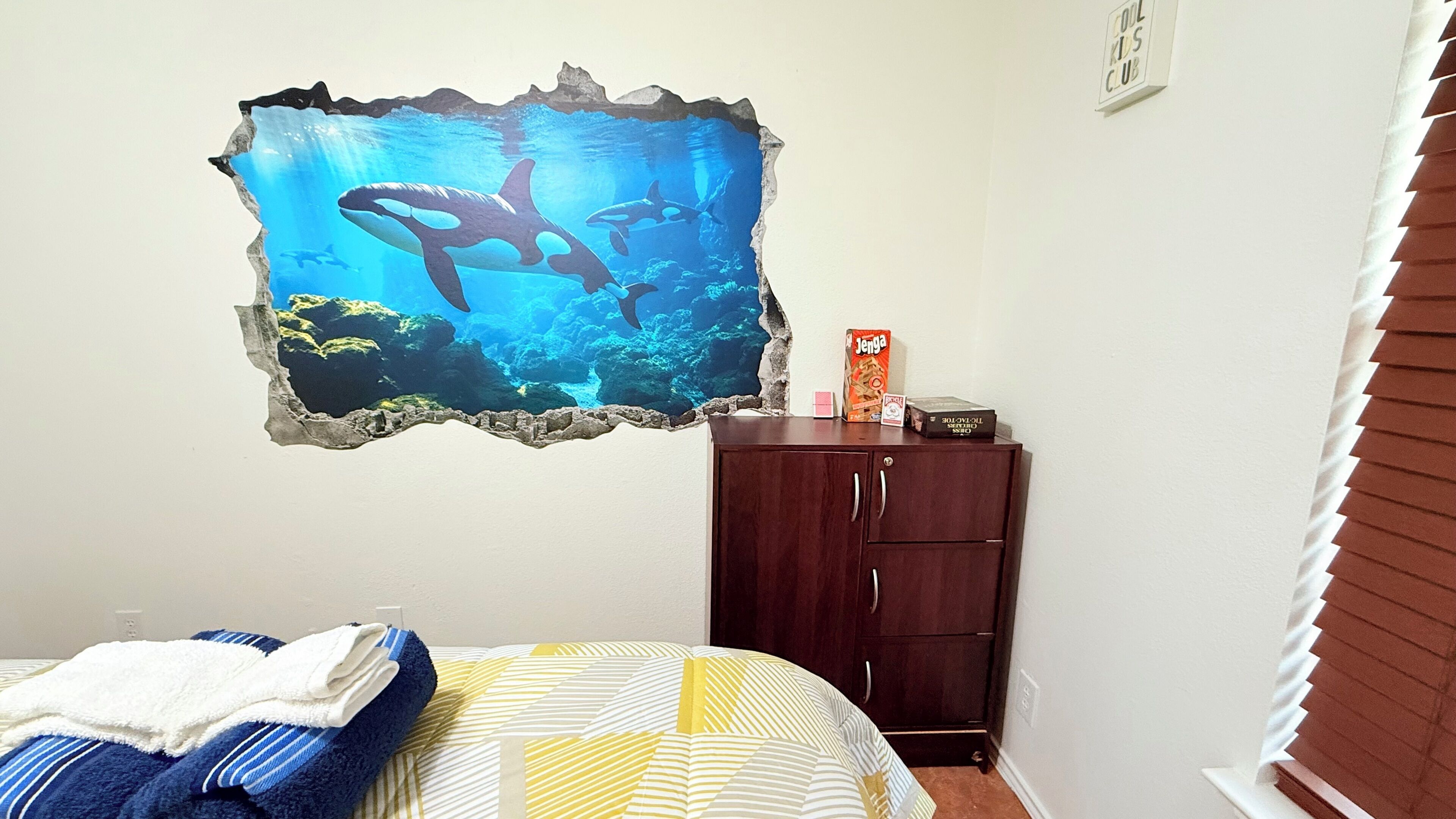 Een slaapkamer met een bed, een dressoir en een muurstickers met een onderwaterlandschap.