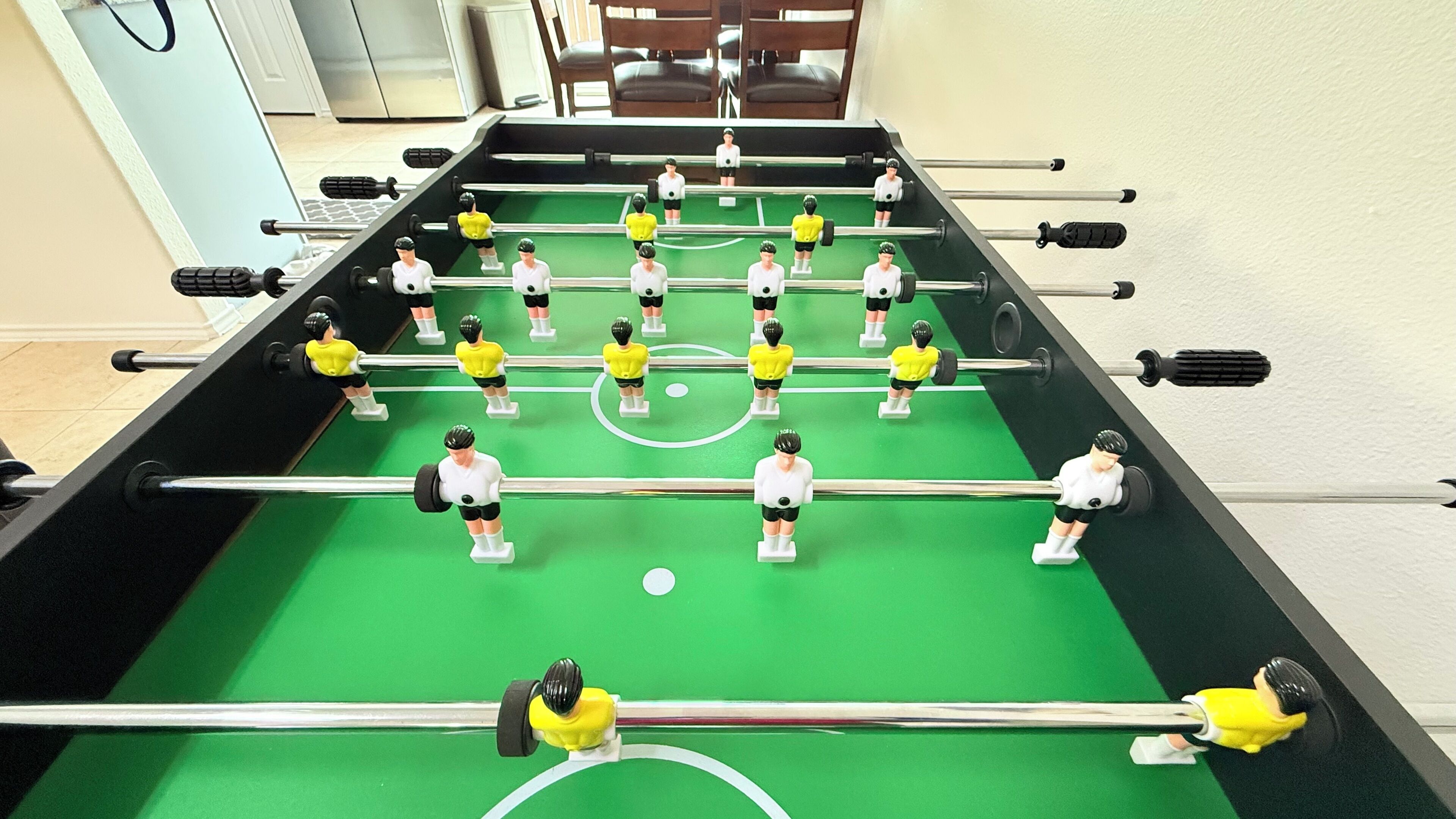 Una mesa de fútbolín con jugadores uniformados en amarillo y blanco, sobre un campo verde.