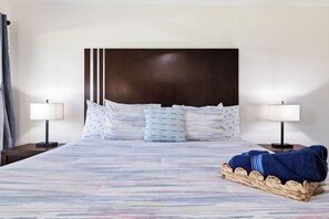 Une chambre d’hôtel avec un grand lit, deux tables de chevet avec des lampes, une tête de lit et un panier en osier contenant une couverture.