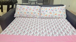 Een bed met beddengoed met bloemen en een torentjespatroon van de Eiffeltoren, een zwarte bank en een tafelvoetbaltafel in een kamer met een betegelde vloer en een stoel.