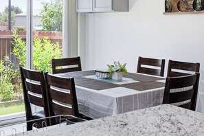 A dining area with a table set for four, surrounded by chairs, a window with a view of greenery, and a kitchen area with cabinets and a countertop. - 🌟 Perfect Stay for BMT Graduation • 5 Min to Lackland AFB & SeaWorld (San Antonio)