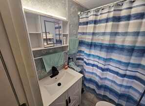 A bathroom with a white sink, a mirror, and a striped shower curtain. - Cumberland Lake House (Nancy)