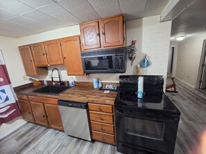 A kitchen with wooden cabinets, a black microwave, a dishwasher, and a stove. - Cumberland Lake House (Nancy)