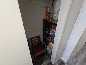 A narrow hallway with a wooden chair and shelves containing board games and a can of paint. - Cumberland Lake House (Nancy)