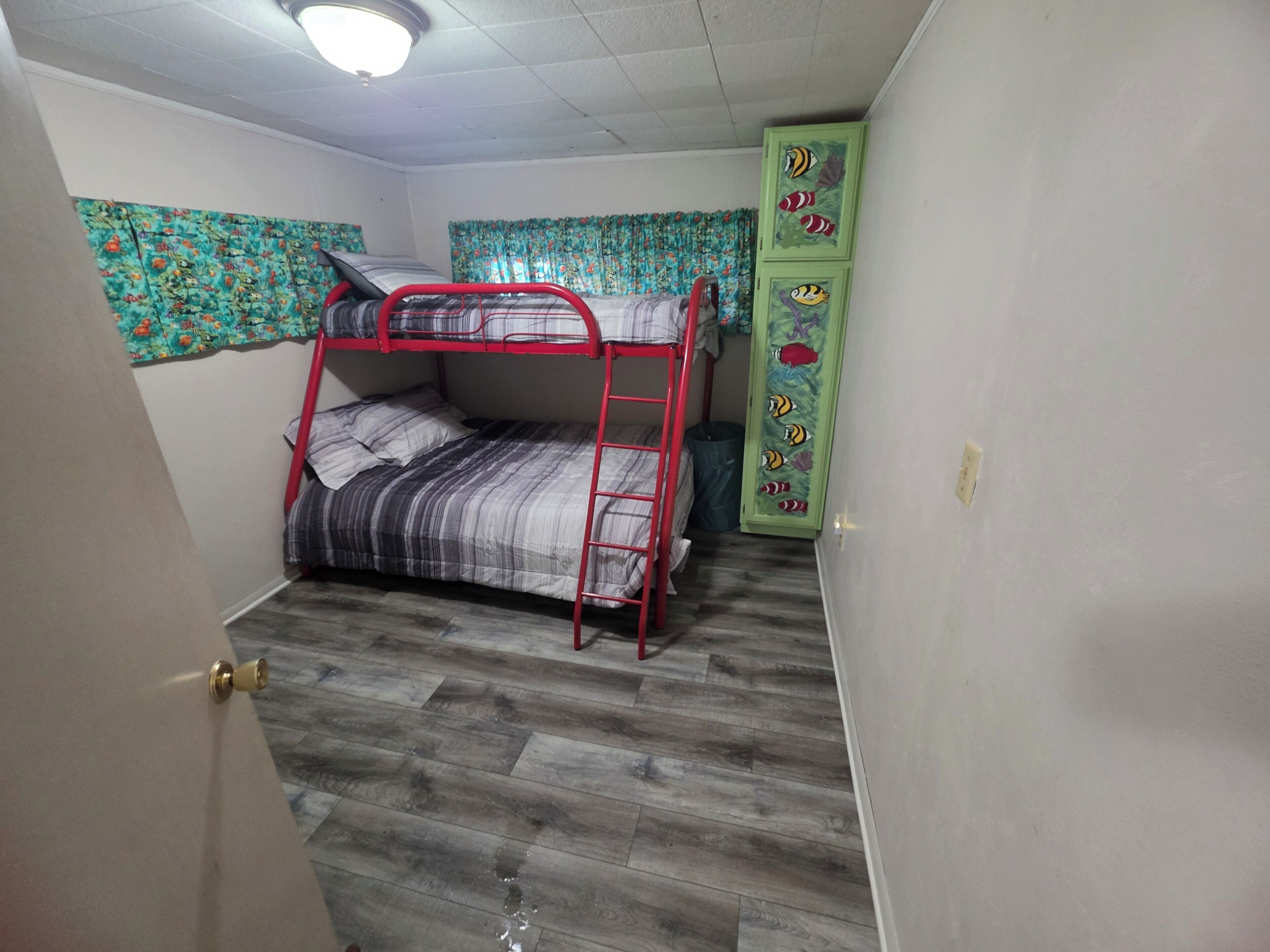 A room with a bunk bed, a green cabinet with fish designs, and patterned curtains.