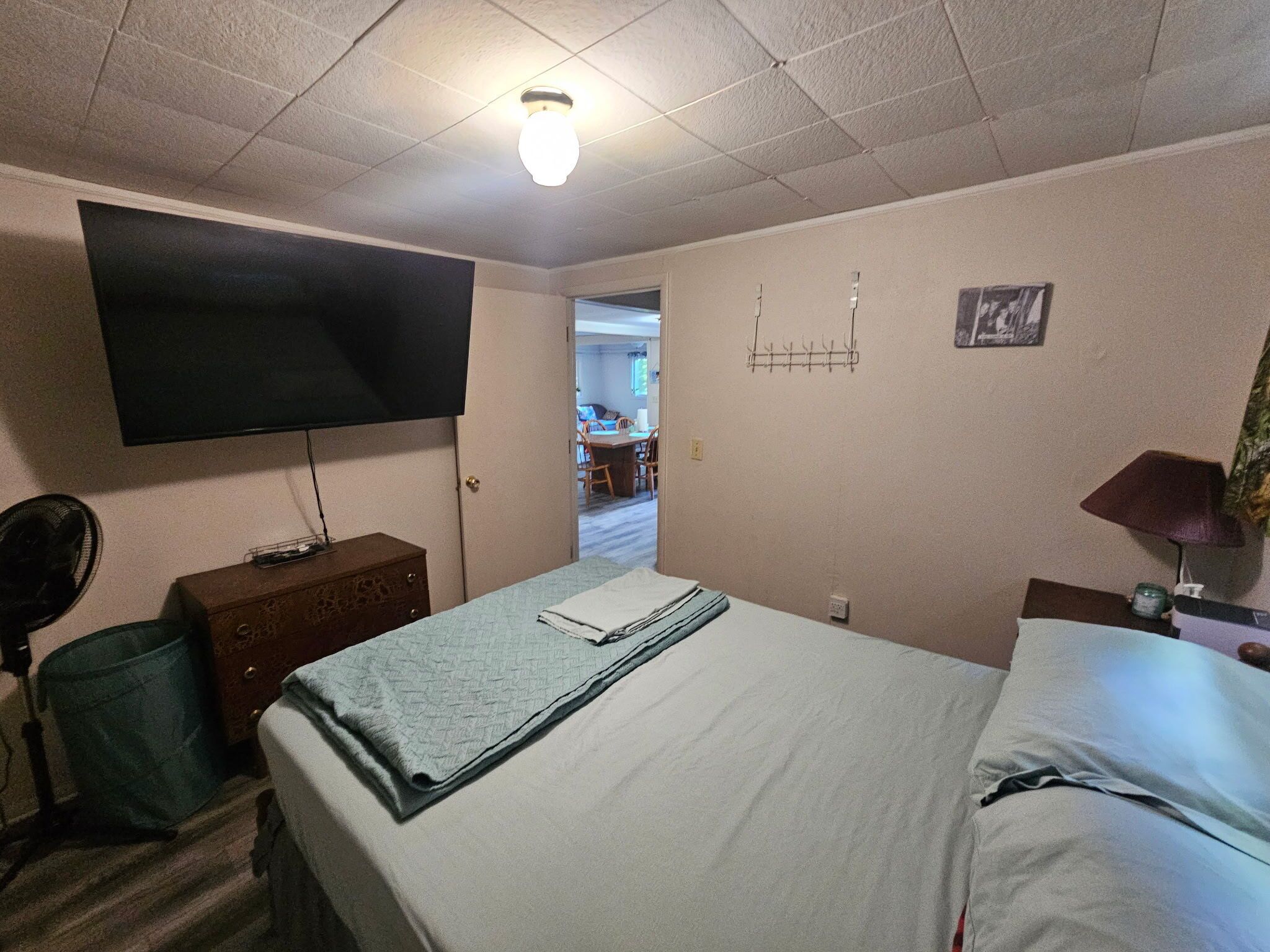 A hotel room with a bed, a television mounted on the wall, a dresser, a desk with a lamp, and a chair.