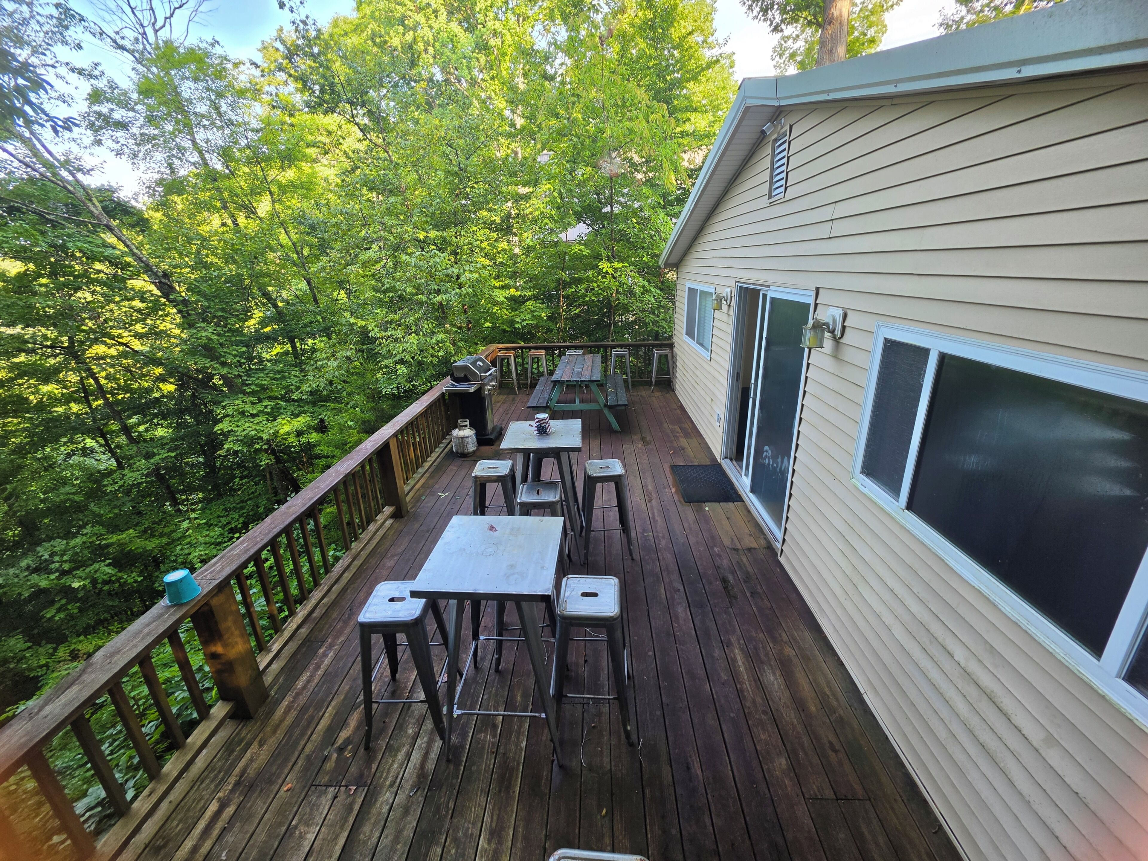 A wooden deck with outdoor furniture, a grill, and a view of a forested area.