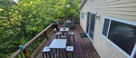 Une terrasse en bois, dotée de mobilier d’extérieur, d’un barbecue et offrant une vue sur une zone boisée.