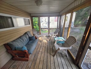 Varanda coberta com piso de madeira, um sofá e cadeiras Adirondack.