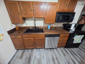 A kitchen with wooden cabinets, a stainless steel dishwasher, a black microwave, and a stove. - Cumberland Lake House (Nancy)