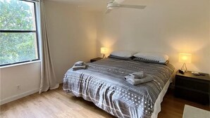 Ein Schlafzimmer mit einem Bett, zwei Nachttischlampen, einem Deckenventilator und einem Fenster mit Vorhängen.