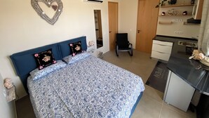 Une chambre avec un lit, une chaise, un bureau et un coin cuisine.