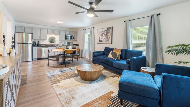 A modern kitchen with stainless steel appliances, a dining area with a round wooden table, a blue sofa set, and a ceiling fan. - Modern Charming 3BR/2BA Home. Walking distance to Downtown Benton & Tyndall Park (Benton)
