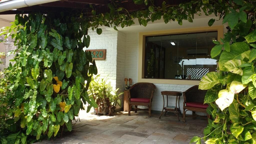 A covered patio area with a white brick wall, a large window, and two wicker chairs with red cushions.