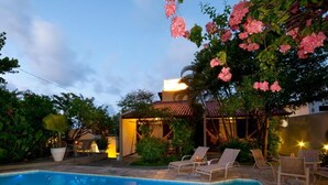 Une piscine entourée de chaises longues, bordée d’une végétation luxuriante et agrémentée d’un patio bien éclairé.