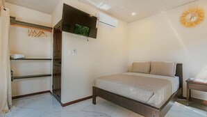 A bedroom with a bed, a TV mounted on the wall, a wardrobe, and a small table.