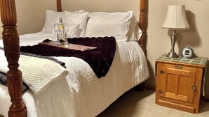 A four-poster bed with a white bedspread and a dark throw blanket, a bedside table with a lamp, and a small wooden cabinet. - Charming 2-bedroom bacement with WiFi, AC in enjoyable Murray (Murray)