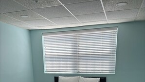 Une chambre à coucher comprenant un lit, deux tables de chevet, une fenêtre avec des stores et un plafond orné d’un motif en réseau.
