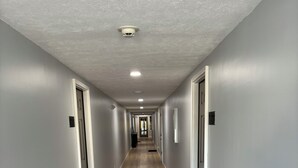 Un long couloir étroit aux murs de couleur gris clair et au plancher en bois, qui mène à une porte au fond.