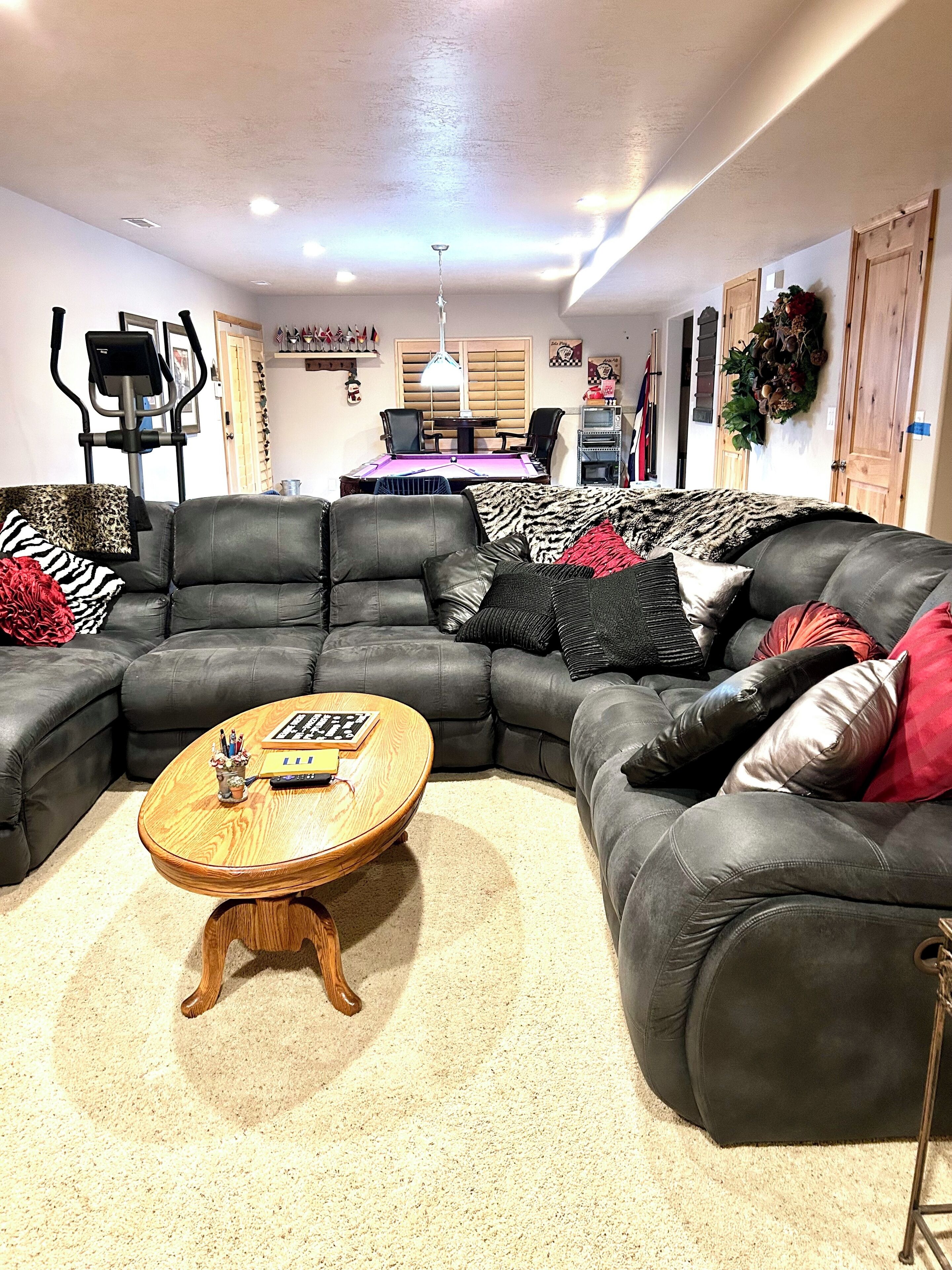 Uma sala de estar com sofá seccional, uma mesa de centro redonda e uma mesa de bilhar ao fundo.