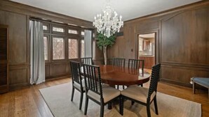 A dining room with a wooden table and chairs, a chandelier, and large windows.