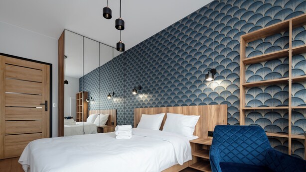Una habitación de hotel moderna con una cama grande, un armario de madera, un sillón tapizado en azul y una pared con estampado.