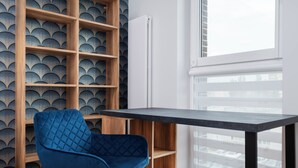 Una habitación con una silla azul, una estantería de madera y una ventana con persianas.