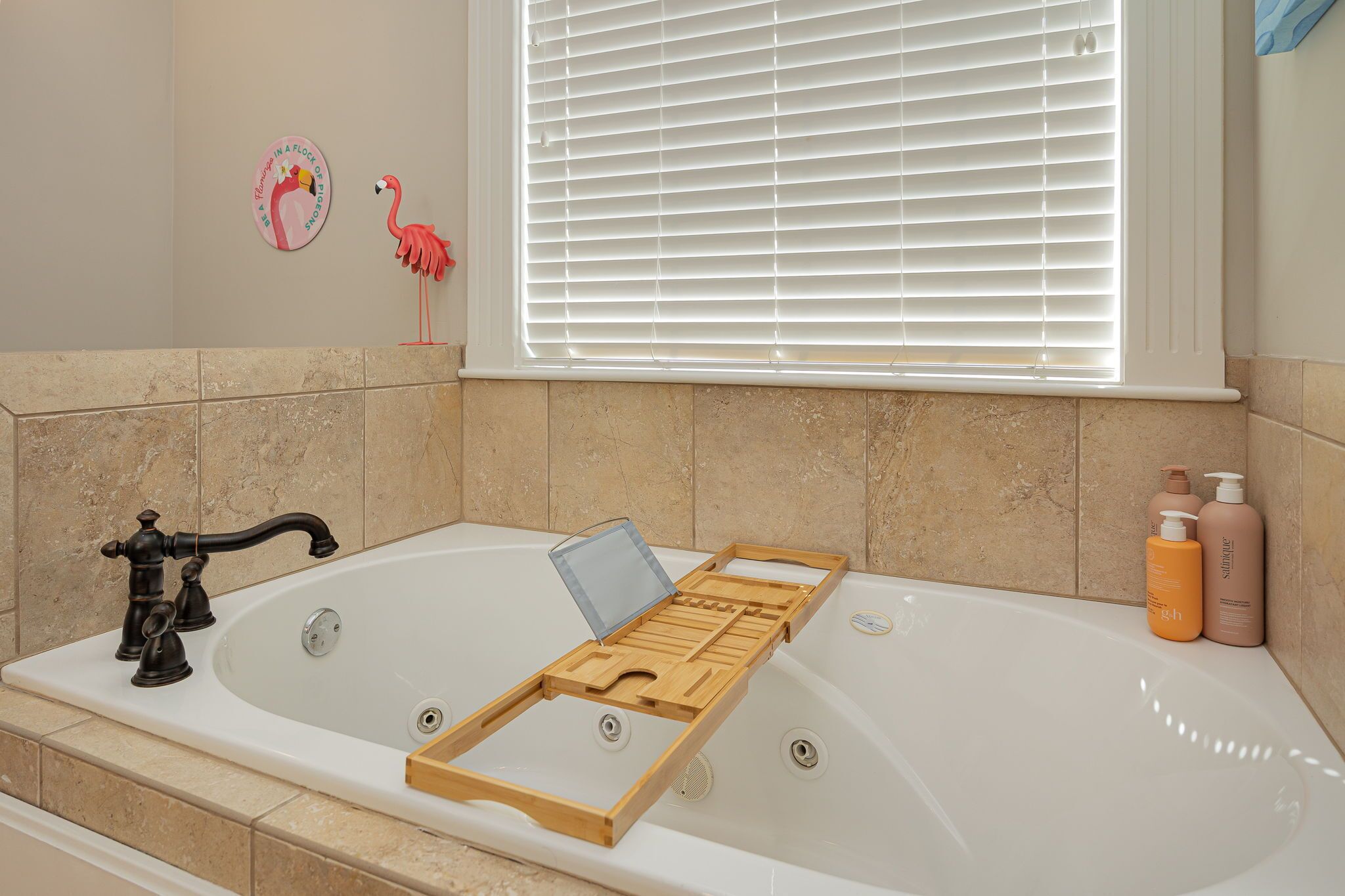 A bathroom with a bathtub, a wooden tray, and two bottles of shampoo.