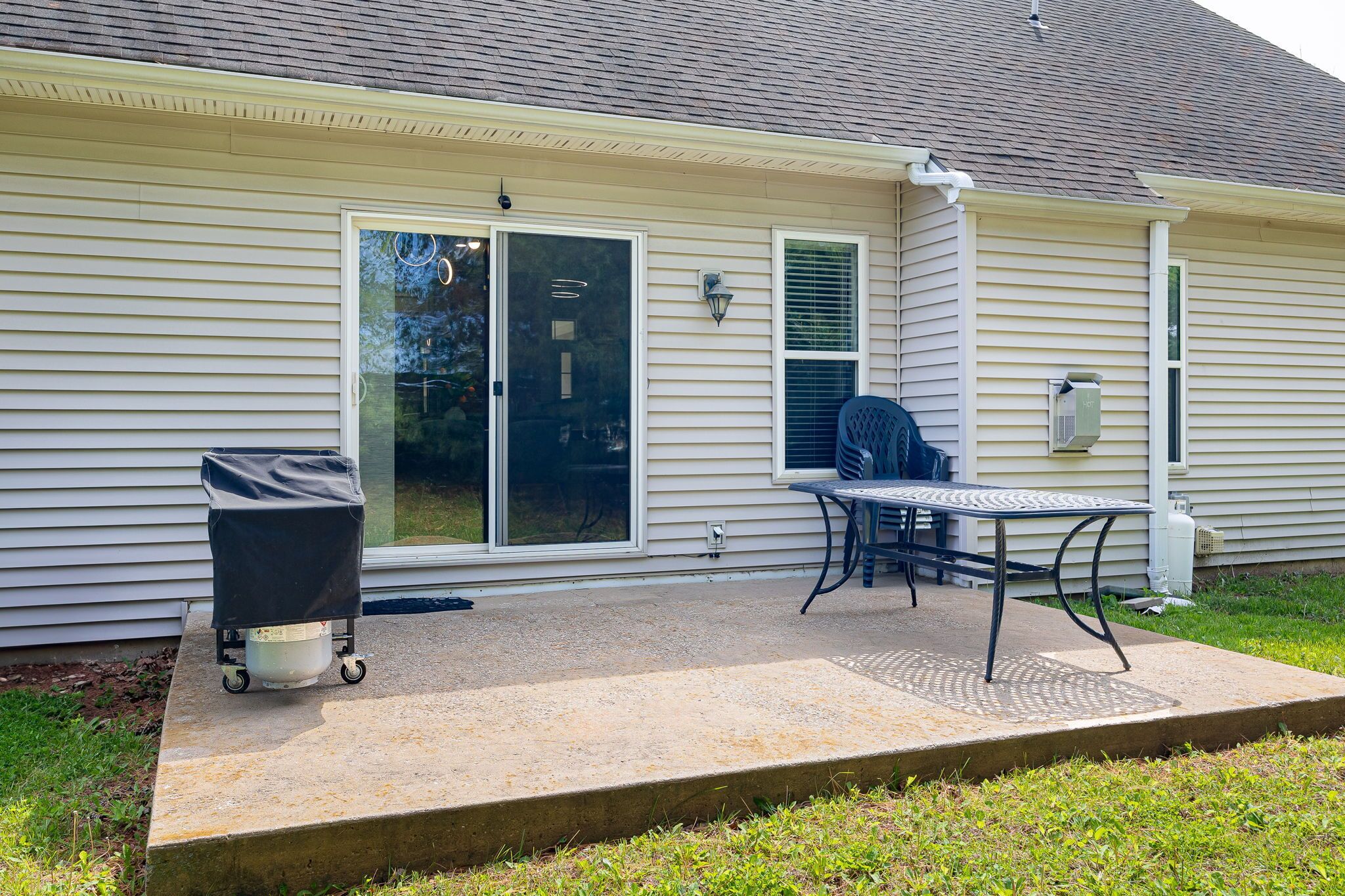 A house with a covered patio, a grill, and a table with chairs.
