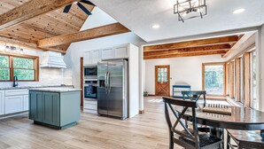A spacious kitchen with wooden beams, a large island, and a dining area with a table and chairs. - Spacious Retreat Near Norman Close to OU & Riverwind Casino (Blanchard)