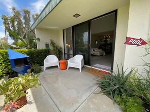 Eine Terrasse mit zwei weißen Stühlen, einem kleinen orangefarbenen Hocker und einer blauen Konstruktion. Ein Schild weist auf ein Schwimmbecken hin.