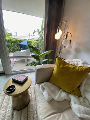 Un salon moderne avec un canapé, une table basse et une vue sur un balcon agrémenté de plantes et orné d’une structure bleue.