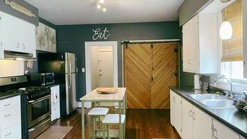 Une cuisine moderne avec des meubles blancs, une porte en bois à motifs en chevrons, un coin repas avec des tabourets et un plan de travail avec un évier.