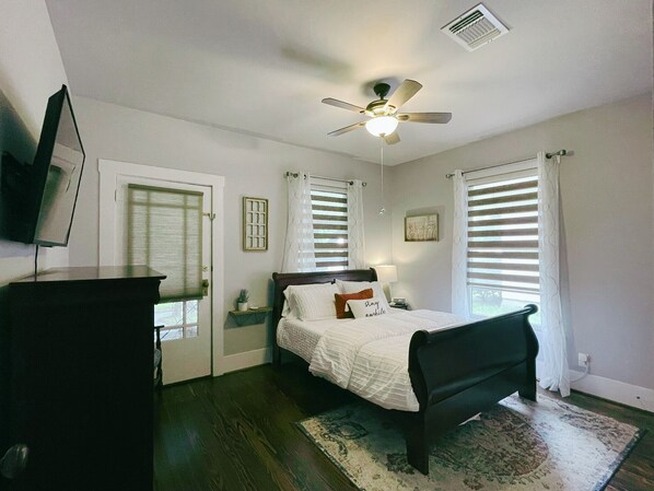 A bedroom with a bed, a ceiling fan, a TV, and a window with blinds.