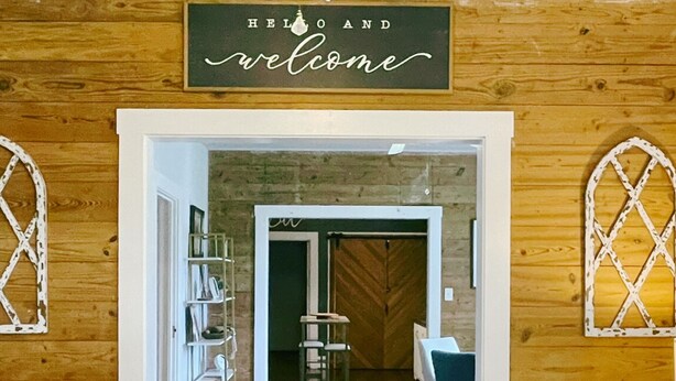 A wooden interior with a 'HELLO AND welcome' sign, a reception desk, and a seating area with a blue chair. - The Baum Suite: Charming 1950s Gem in Schulenburg ~New Owner~ (Schulenburg)