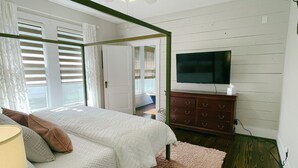 A bedroom with a bed, a TV, a dresser, and a window with blinds. - The Baum Suite: Charming 1950s Gem in Schulenburg ~New Owner~ (Schulenburg)