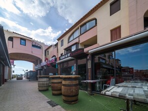 Una calle con barriles de madera, un restaurante llamado "RESTAURANT BAR TAPAC" y un letrero que dice "LE CHAT ROUGE".
