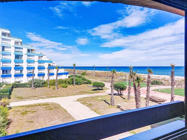 Un hotel frente al mar con varios pisos, vistas a la playa y palmeras.