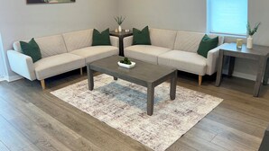 Una sala de estar moderna con un sofá seccional color beige, una mesa de centro de madera y una alfombra estampada.