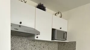 Une cuisine compacte avec des meubles blancs, un four à micro-ondes, une machine à café et un grille-pain.