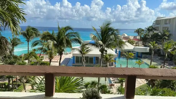 Un balcon avec vue sur l’océan, les palmiers et l’espace piscine.