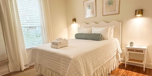 Une chambre à coucher comprenant un lit, une table de chevet, une fenêtre avec des stores et un luminaire fixé au mur.