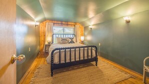 A bedroom with a bed, wooden walls, a window with curtains, and a nightstand with a lamp. - Beach Cottage w/ Water Access (Port Ludlow)