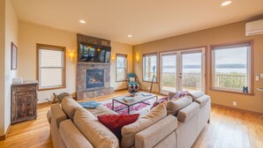 A spacious living room with a fireplace, large windows, and a view of the outdoors. - Waterfront Home w/ Beach access! (Port Ludlow)
