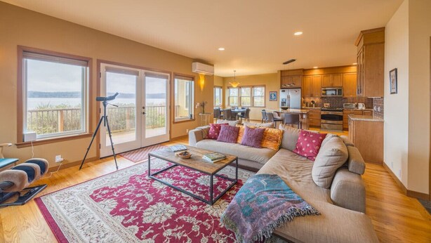 A spacious living room with a large sofa, a coffee table, and a view of the outdoors through sliding glass doors. - Waterfront Home w/ Beach access! (Port Ludlow)