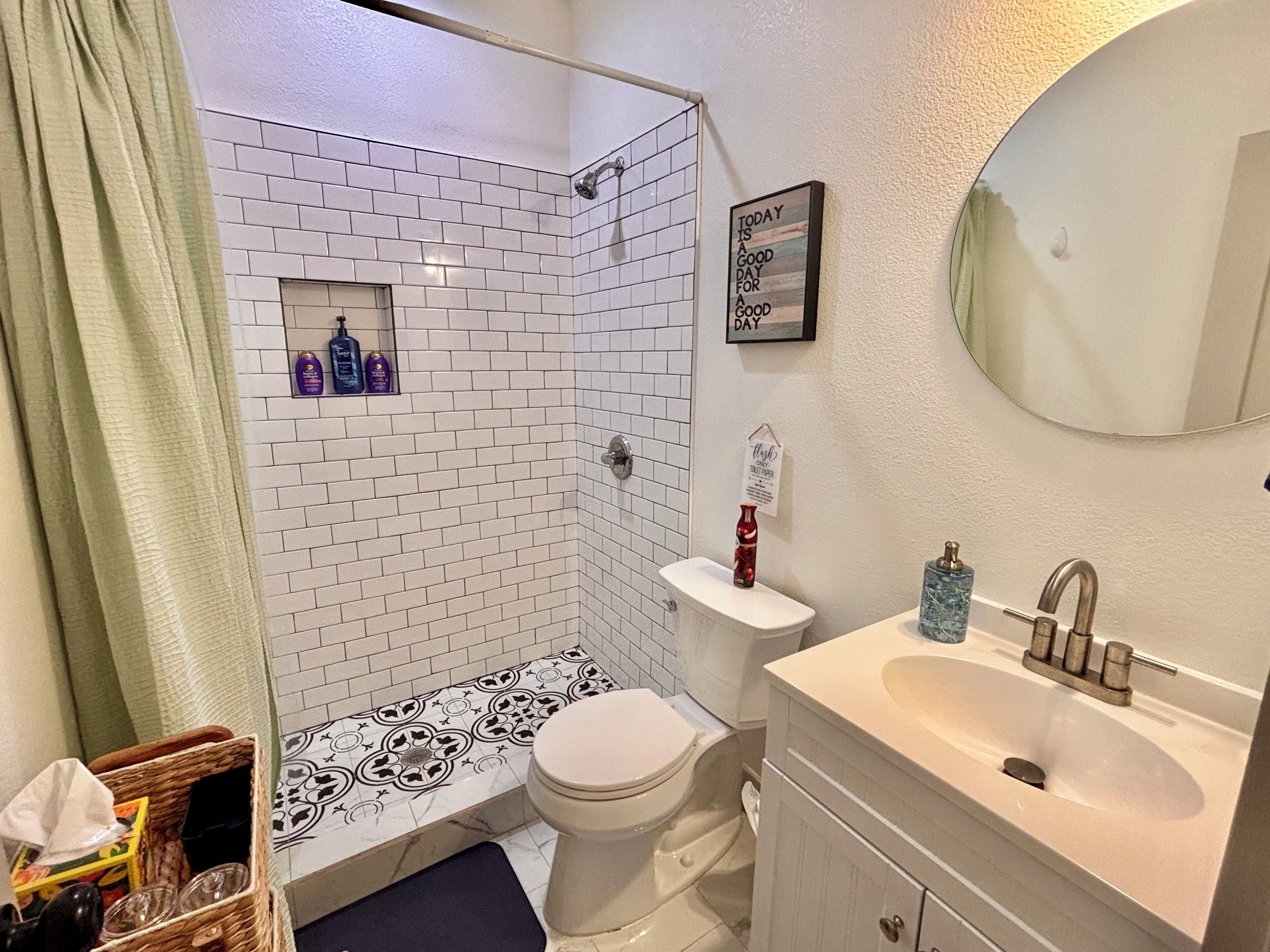 A bathroom with a shower, toilet, and sink. There are toiletries on the wall and a basket of items on the floor.