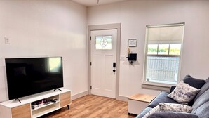 Een woonkamer met een televisie op een witte kast, een grijze bank en een houten vloer.