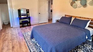 Een slaapkamer met een groot bed, een bureau met stoel, een spiegel en een deur die naar een andere kamer leidt.