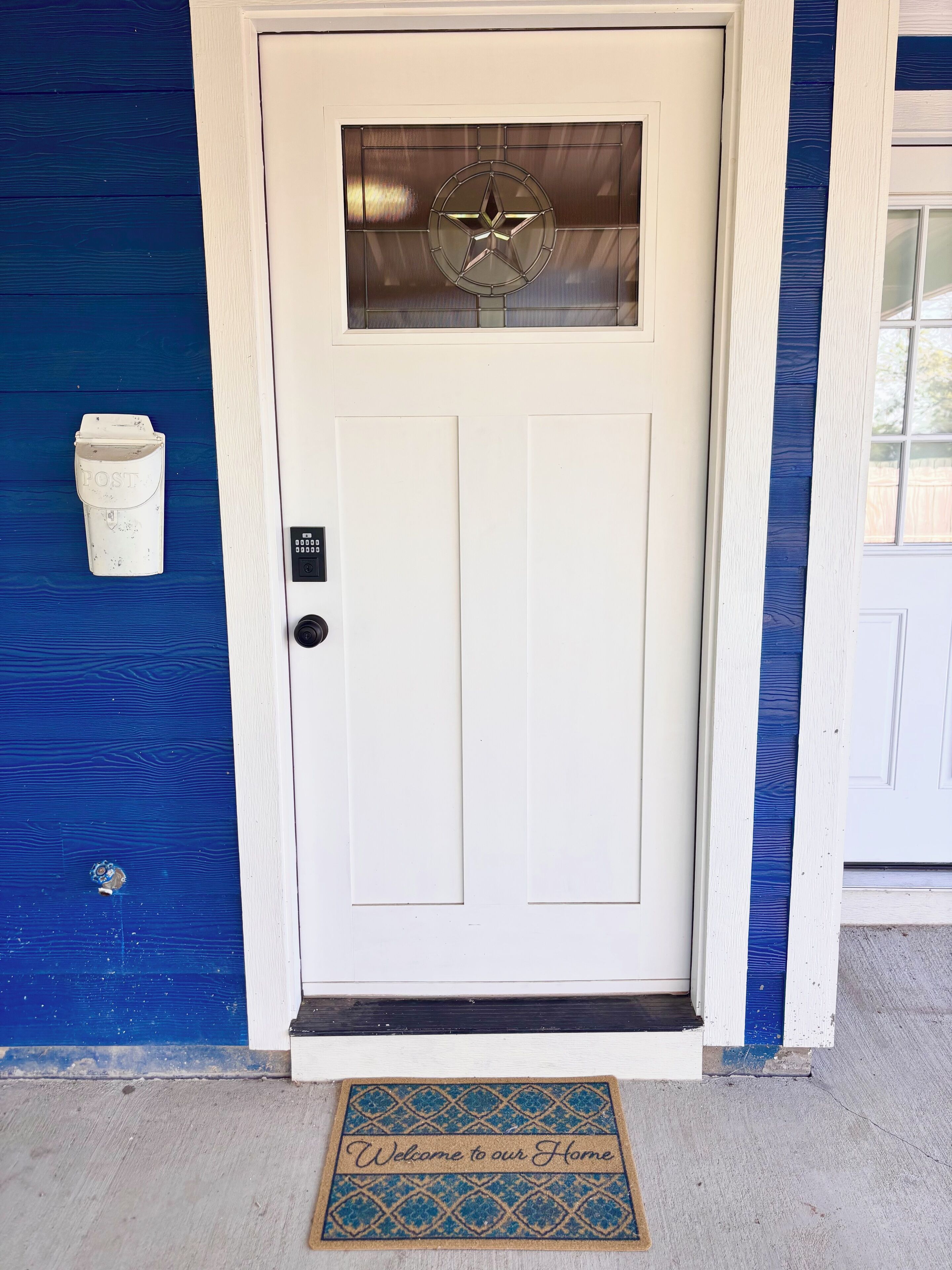 A white door with a star-shaped window, a mailbox, and a welcome mat.